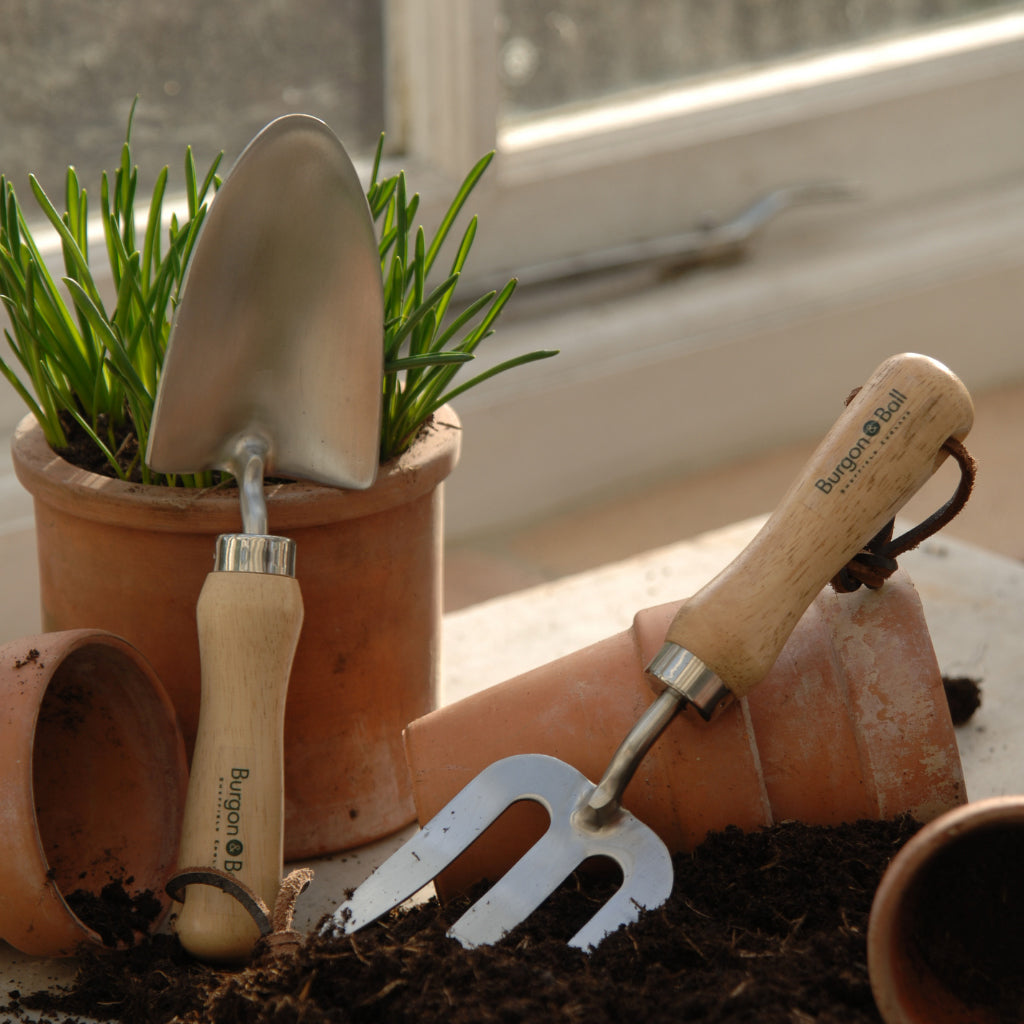 Burgon & Ball children's hand trowel and fork on a table with pots and soil
