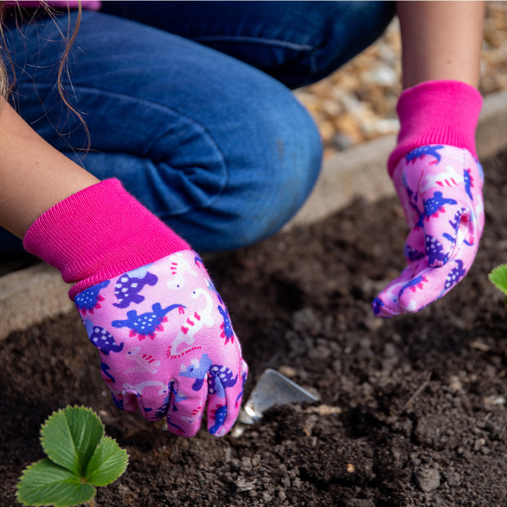 Child wearing Kent and Stowe gardening gloves in pink with dinosaurs while planting