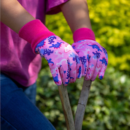 Child wearing Kent and Stowe gardening gloves in pink and blue while using digging tool