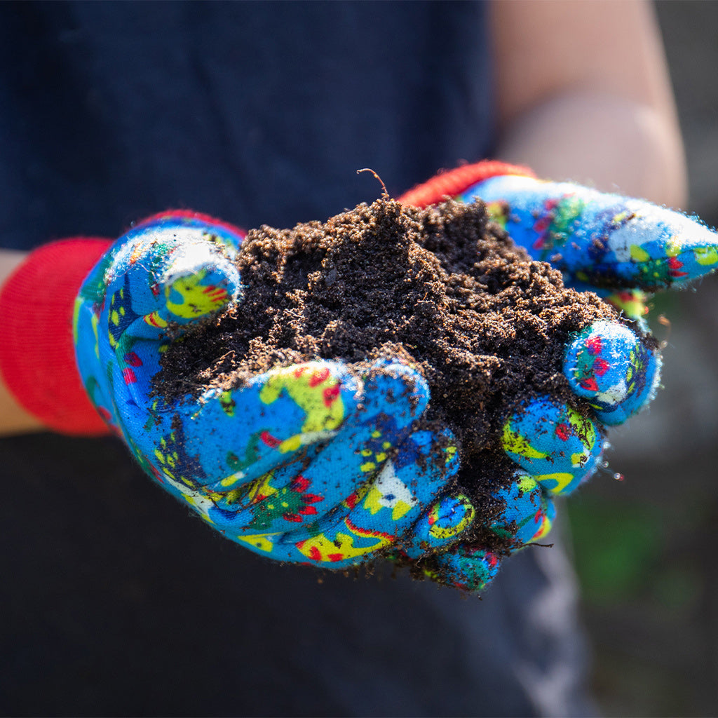 Child holding soil using Kent and Stowe gardening gloves for kids in blue with dinosaurs